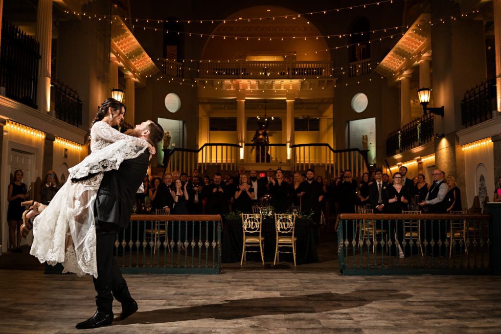 groom lifting bride in dark reception venue for their first dance