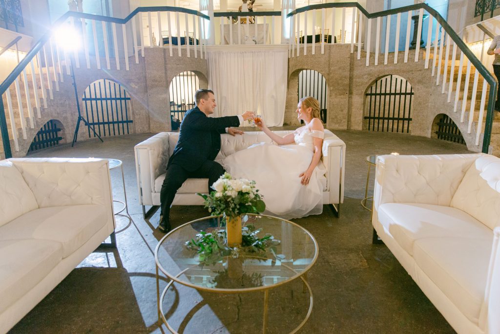 bride and groom sharing a private toast on white couches