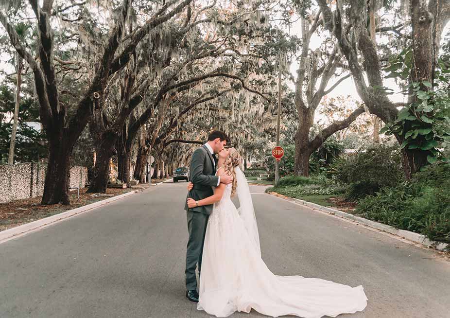 Bride and groom kissing in the middle of the street while mature trees hang over them