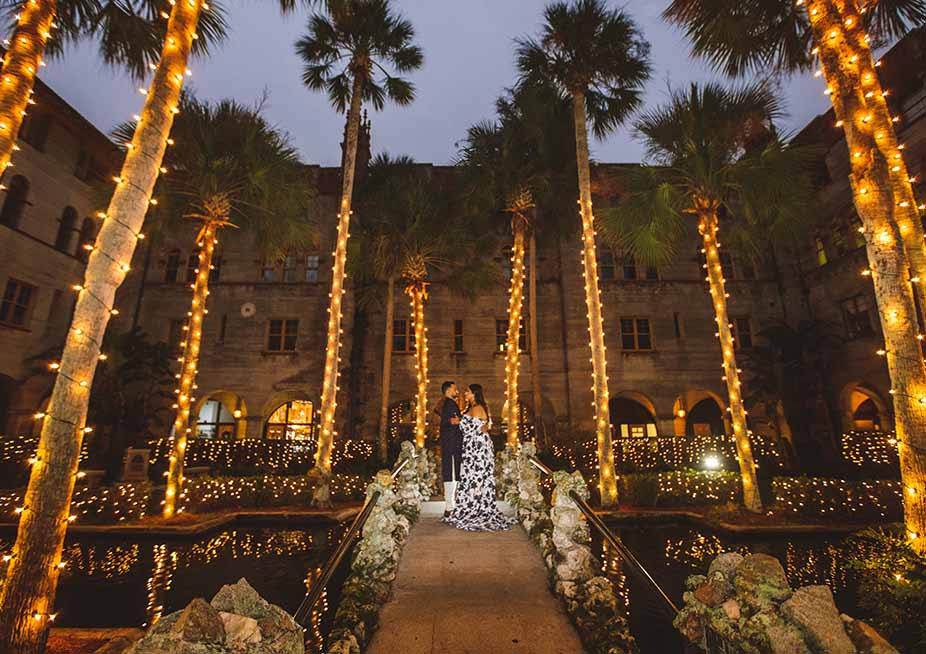 Outside The Lightner Museum at night. The palms are lit up with warm lights and a couple is dancing beneath them.