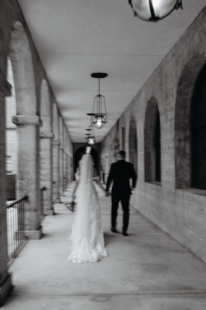 Black and white photo of bride and groom walking outside Lightner Museum