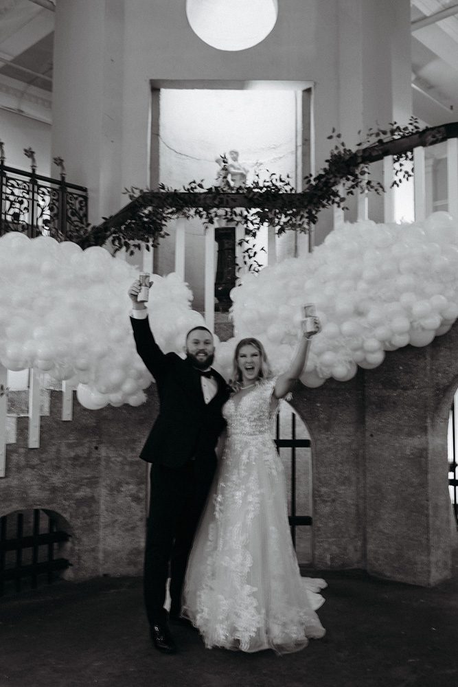 Black and white photo of bride and groom under balloon angel wings