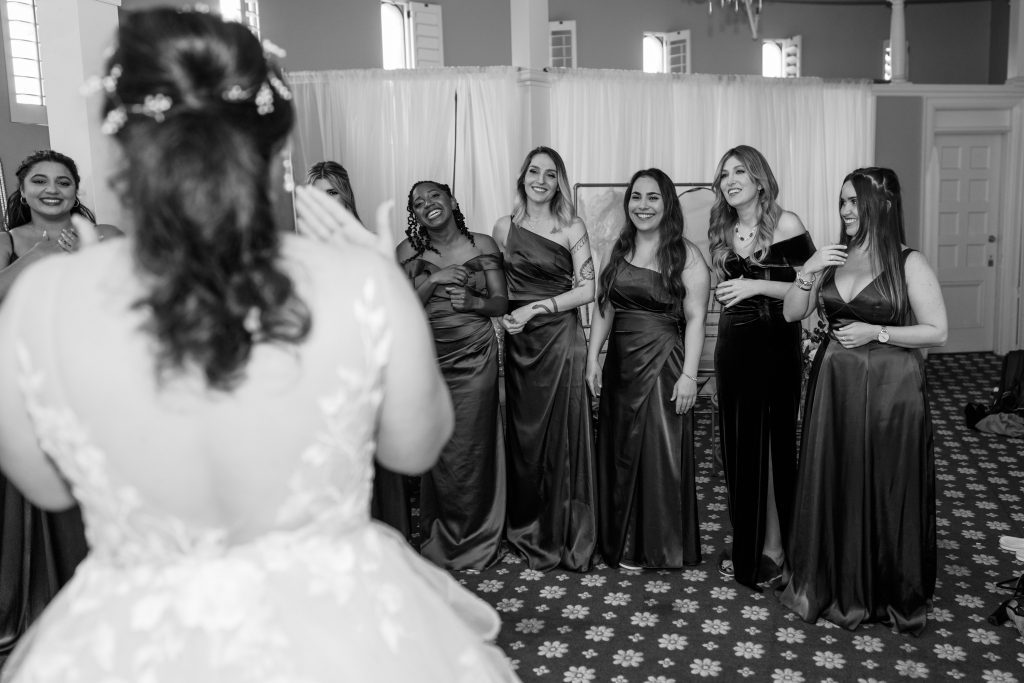 black and white image of Cory showing her bridal gown to her bridesmaids
