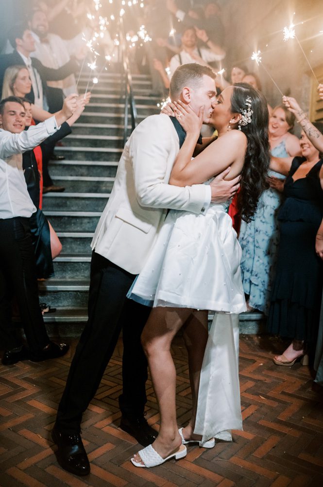 Bride and groom kiss under sparkler exit.
