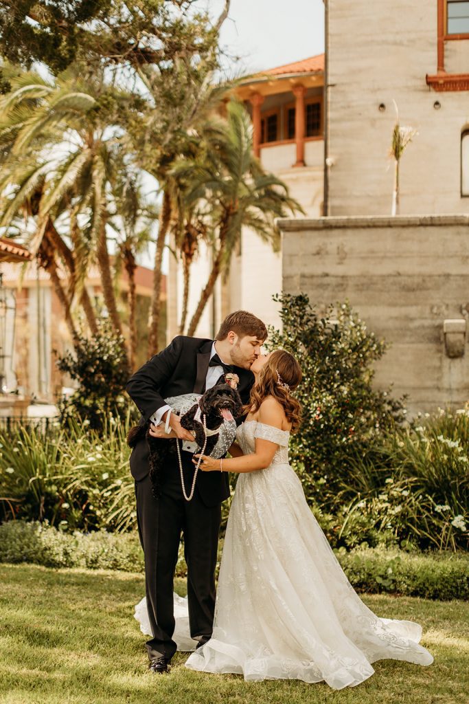 Bride and groom kiss while groom holds dog