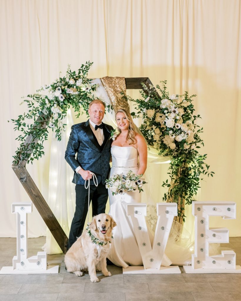 bride and groom standing next to giant letters spelling out LOVE with their dog as the O