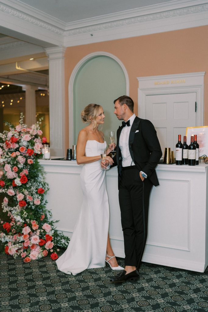 bride and groom posing next to wedding bar decorated with colorful floral arrangement
