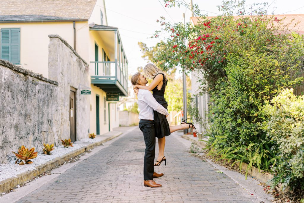 man lifting fiancee on the cobblestone streets of St. Augustine