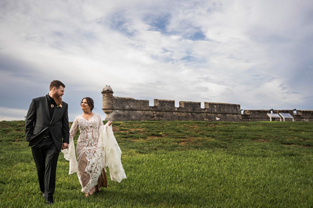 Bride and groom walking in field with fort behind them