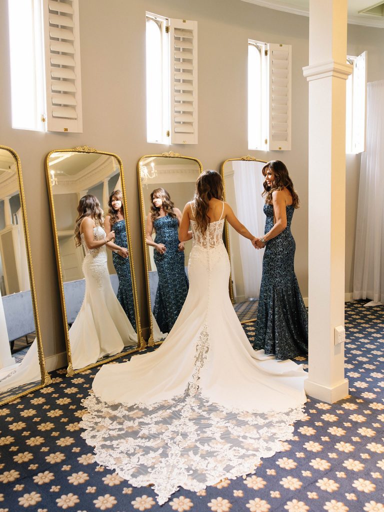 Bride hold hands with mother in front of mirrors in bridal suite